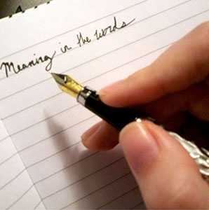 Alese's hand holding a dip pen over a notebook page on which she has written 'Meaning in the words' in cursive